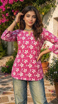 Woman wearing a pink floral blouse with blue jeans standing outdoors.