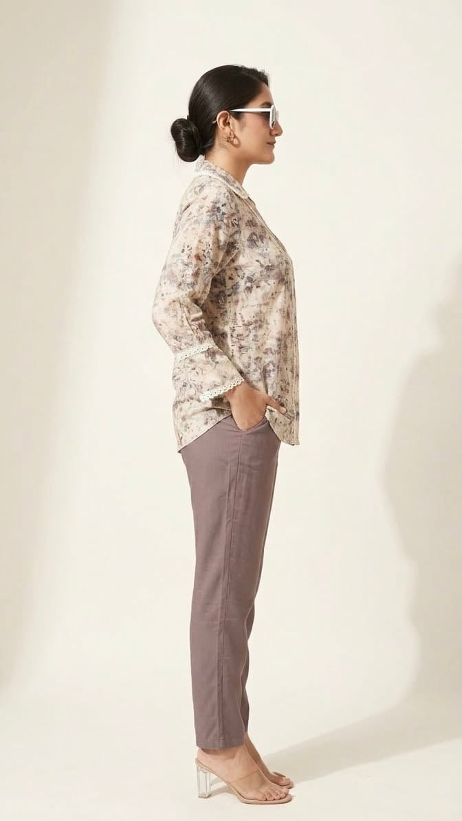 Woman wearing a patterned blouse and gray pants against a white background