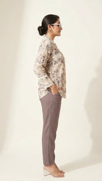 Woman wearing a patterned blouse and gray pants against a white background