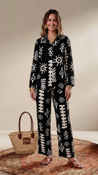 Woman wearing a black and white patterned outfit with a woven bag on a beige background