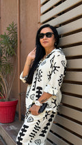 Woman wearing a white outfit with black patterns against a wooden background