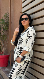 Woman wearing a white outfit with black patterns against a wooden background