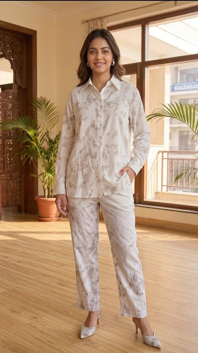 Woman in a light-colored outfit standing in a room with wooden flooring and large windows.