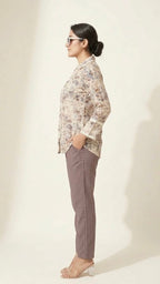 Woman wearing a floral blouse and gray pants on a plain background