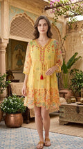 Woman in a yellow dress standing in an ornate indoor setting with plants and decorative elements.