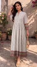 Woman in a long, patterned dress standing outdoors with plants and flowers in the background