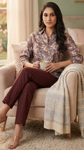 Woman sitting on a couch holding a mug, wearing a patterned top and brown pants.